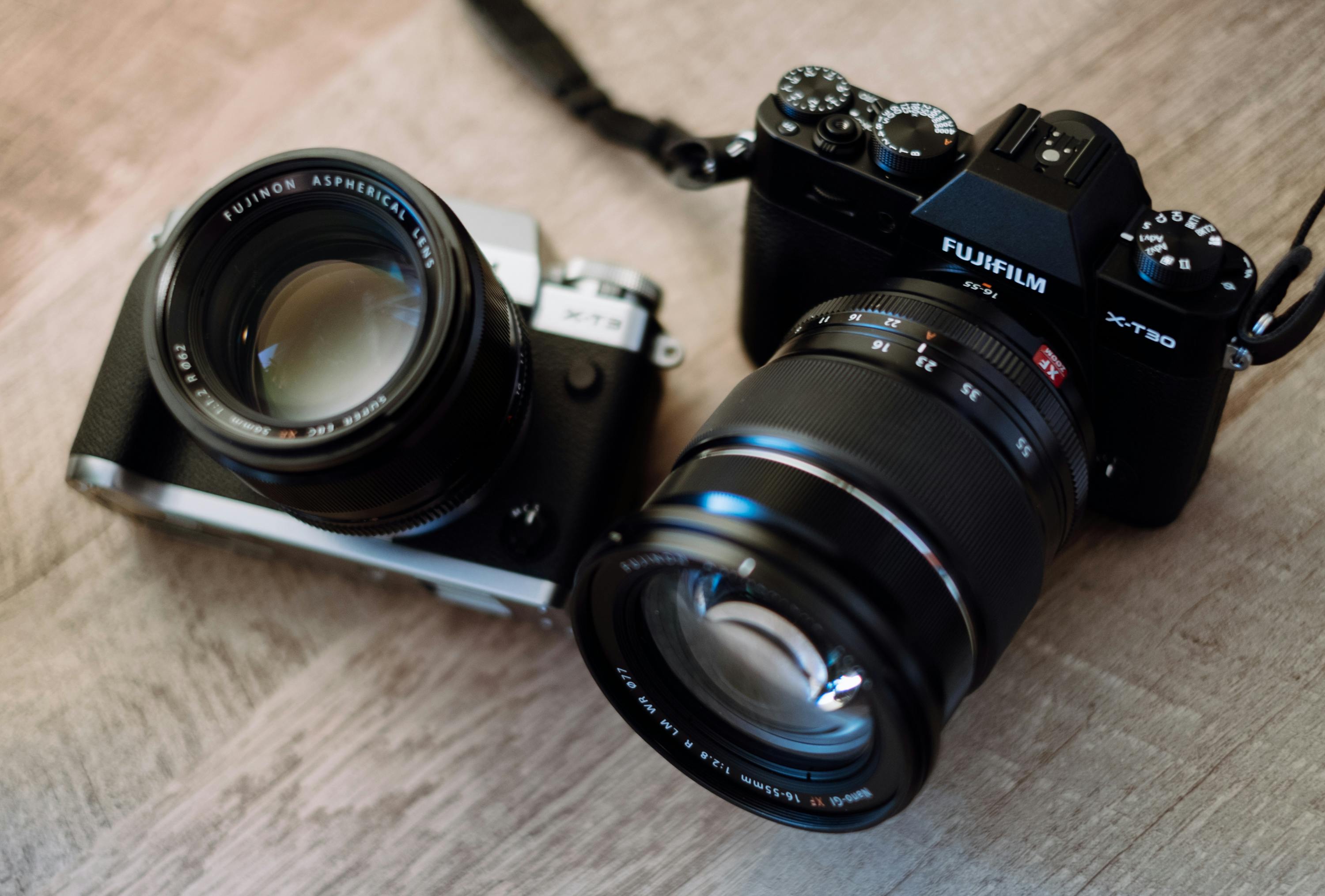 Detailed view of two Fujifilm cameras on a wooden surface, showcasing lenses and dials.